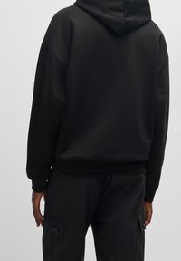 Sudadera negra con capucha de corte relajado, textura suave y puños acanalados. Presenta un diseño limpio sin patrones visibles ni elementos metálicos.