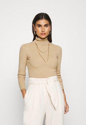 Beige ribbed turtleneck sweater with long sleeves, paired with high-waisted cream pants featuring a belted tie. Gold layered necklace.