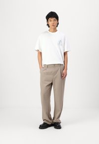 White cotton t-shirt with graphic print, paired with loose-fitting beige trousers and black platform shoes, against a plain white background.