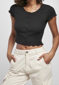Černý žebrovaný cropped top s krátkými řasenými rukávy a zapínáním na knoflíky, kombinovaný s béžovými cargo kalhotami s vysokým pasem.
