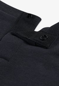Sort ribbet stof med knaplukning detaljer. Har en blød tekstur og struktureret design, der fremhæver syninger og stoffolder.