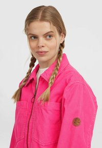 Roze corduroy jas met een rits aan de voorkant, twee voorzakken en een ronde logo patch op de linker mouw. Zachte textuur en een warm ontwerp.