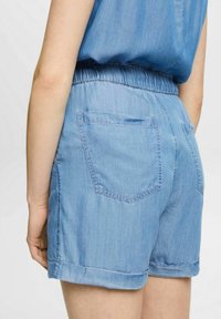 I pantaloni corti in denim blu chiaro presentano una vita elastica e orli arrotolati, con due tasche posteriori e una texture liscia.