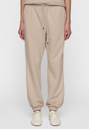 Pantaloni della tuta beige con vita regolabile mediante cordino, polsini elastici e dettagli a strisce laterali. Realizzati in materiale morbido, presentano una vestibilità comoda.