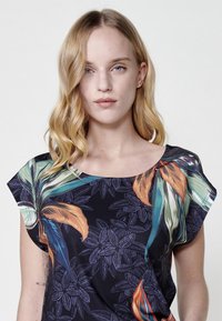 Haut fleuri à manches courtes avec un fond bleu foncé, des motifs de feuilles orange vif et vert, et un col rond. Texture de tissu lisse.