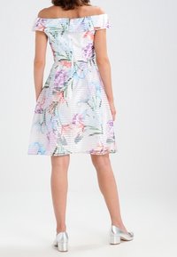 Kwiatowa sukienka bez ramiączek z lekkiego materiału w poziome paski, w pastelowych kolorach i dopasowanym topie. Srebrne buty na blokowym obcasie.