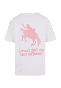 Biela bavlnená tričko s ružovou grafikou kovboja na koni a textom "Kovboji nespia. Kofeínujú." pod ním.