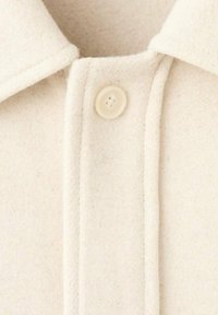 Camicia color crema in lana con chiusura a bottoni, colletto e dettagli di cucitura visibili. Texture morbida con una finitura liscia.