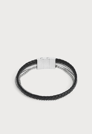 Bracelet en cuir tressé noir avec deux chaînes en argent et un fermoir magnétique rectangulaire en argent.