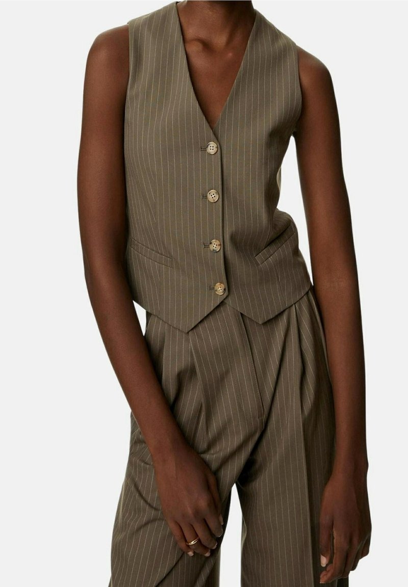 Oliwkowa kamizelka w prążki z dekoltem w serek, zapięciem na pięć guzików i bocznymi kieszeniami. Wykonana z teksturowanej tkaniny, dopasowany krój.