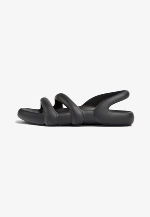 Black slip-on sandals featuring a wavy, sculptural design. Made from smooth, flexible material with a textured sole for grip.