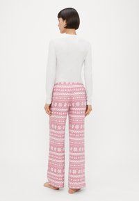 Garām piedurknēm balta blūze kopā ar izplestām rozā pidžamas biksēm ar baltu ziedu un ziemas rakstu dizainu. Mīksts audums, ērtas piegriezums.