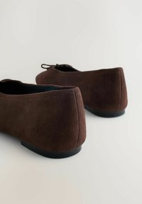 Barna szarvasbőr balettcipő alacsony, kerekített sarokkal. Simább textúrával, elegáns kialakítással és kis masni díszítéssel a felső részen.