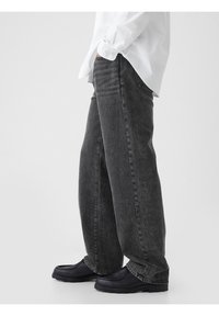 Jean gris foncé à jambes larges en denim à la texture douce. Présente un délavage subtil, des détails cousus et une coupe décontractée.