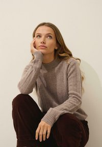 Jasnobrązowy prążkowany sweter z wysokim kołnierzem, połączony z ciemnobrązowymi spodniami z kordurowej tkaniny. Gładka faktura i luźny krój.