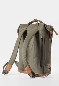 Zaino a scomparsa verde oliva con base in pelle, spallacci regolabili, tasca frontale con zip e dettagli in pelle marrone chiaro. Finitura in tela texturizzata.