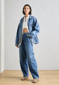 Ljusblå denimjacka med oversized passform, tillsammans med högmidjade, löst sittande jeans med lappar; krämfärgad topp under.
