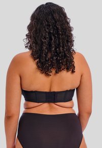 Soutien-gorge bandeau noir avec fermeture à crochets, fabriqué en tissu lisse et à la conception simple. Sous-vêtements noirs taille haute, surface texturée, style minimaliste.