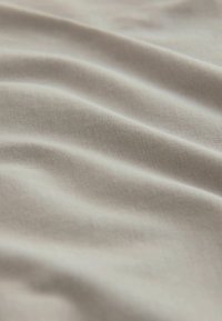 Svijetlosmeđi materijal s glatkom, teksturiranom površinom i blagim nabora, koji prikazuje mekani, tkaninski izgled.