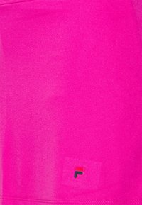 Top deportivo de color rosa brillante hecho de tela suave. Cuenta con un pequeño logo multicolor en la esquina inferior. Diseño simple y ajustado.