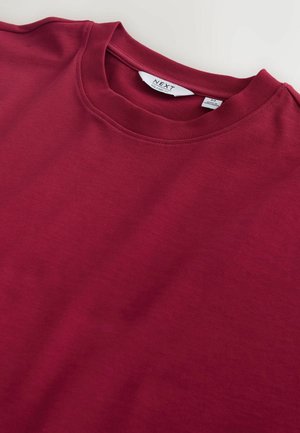 Vīnsarkanā kokvilnas T-krekls ar apaļu kakla izgriezumu un īsām piedurknēm, ar gludu tekstūru un smalkām šuvju detaļām.
