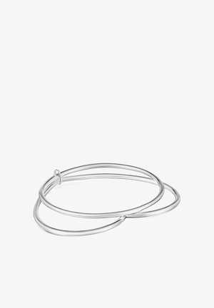 Dwie zazębiające się, gładkie srebrne bransoletki typu bangle bez widocznych zapięć na białym tle.