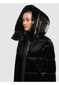 Melna pūkaina jaka ar spīdīgu virsmu, lielu kapuci, rāvējslēdzēju un aizdares ar spiedpogām, kā arī sānu kabatām. Aprīkota ar iesaiņotām sekcijām siltumizolācijai.