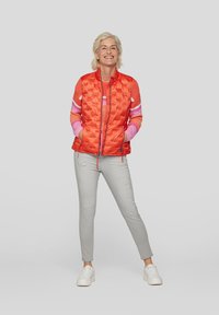 Rote Puffer-Weste mit kariertem Design, Reißverschluss vorne und zwei Taschen, getragen über einem rosa gestreiften Pullover, kombiniert mit hellgrauen Hosen und weißen Sneakern.