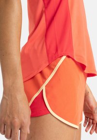 Leistungsorientiertes Sportoutfit mit einem enganliegenden, atmungsaktiven roten Kurzarmshirt und orangefarbenen Shorts mit kontrastierenden Akzenten und einem leichten Design.