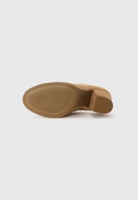 Bottine en suède beige avec un bout arrondi, une semelle en caoutchouc texturé et un talon empilé. Présente des détails de couture subtils le long de l'empeigne.