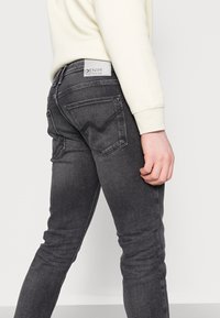 Jean skinny gris foncé avec une texture délavée, doté de coutures sur les poches arrière et d'une étiquette sur la ceinture. Matière en mélange polycoton.