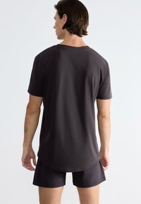 Tmavě šedé tričko s krátkým rukávem vyrobené z bavlny. Má volný střih a zaoblený lem. Pohled zezadu ukazuje hladkou texturu a žádné ozdoby.