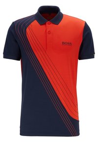 Polo tričko s námořnickým modrým základem a červenými akcenty, obsahující šikmé pruhy a pevný límeček. Materiál vypadá hladce a prodyšně.