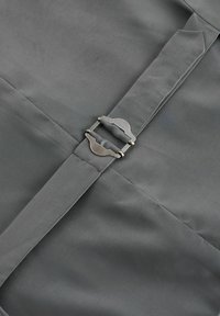 Gros plan d'un tissu gris avec des coutures cousues et une boucle métallique argentée fixée à une sangle grise assortie.