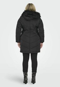 Melnā pūkainā jaka ar kažokādas oderi, ar piegulošu siluetu, teksturētām sānu paneļiem un diagonālo quilt. Nēsāta kopā ar melnām biksēm un papēžkurpēm.