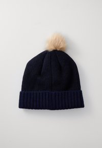 Strikket marineblå lue med ribbet mansjett og en tan fuskepels pom-pom på toppen. Teksturert mønster synlig gjennom hele kroppen.