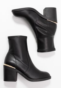 Bottines noires en cuir lisse. Elles présentent un talon bloc avec un accent métallique et un minimalisme dans les coutures. Semelle plate.