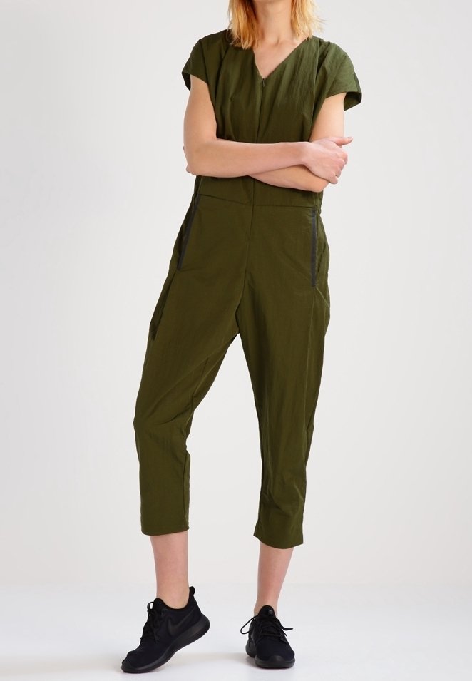 Mono verde olivo con mangas cortas, escote en V, pantalones cortos ajustados, bolsillos laterales y detalles en negro, hecho de un material ligero.