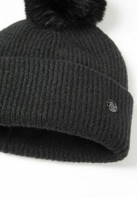 Melna ribota adīta cepure ar lielu melnu mākslīgā kažokādas pom-pom augšā un spīdīgu logo akcentu uz salocītā malas.