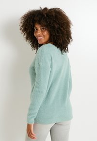 Suéter esponjoso de color verde menta con mangas largas, cuello redondo y un ajuste relajado, combinado con pantalones gris claro. Textura suave y apariencia blanda.