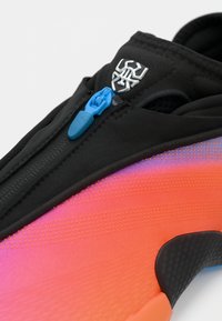 Μαύρο αθλητικό παπούτσι με κλείσιμο με φερμουάρ, πάνω μέρος με διαβάθμιση από πορτοκαλί σε ροζ και υφασμάτινες λεπτομέρειες. Σημαντική λεπτομέρεια σε μπλε μεταλλικό εξάρτημα στο φερμουάρ.