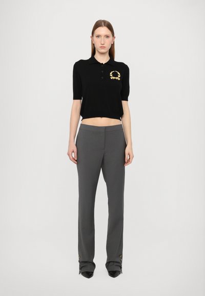 Polo negru scurt cu mâneci scurte și logo brodat auriu, asociat cu pantaloni gri croiți, cu accente de buton la tiv.