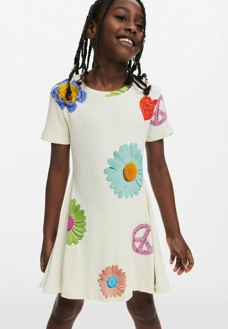 Bijela haljina kratkih rukava s šarenim izvezenim cvjetovima i simbolima mira. Izrađena od rebraste tkanine, s lepršavim, A-linijskim krojem.