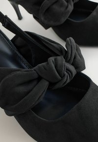 Schwarze Wildleder-Pumps mit einer geknoteten Schleife vorne, runder Zehenform und einem glatten Innenfutter.
