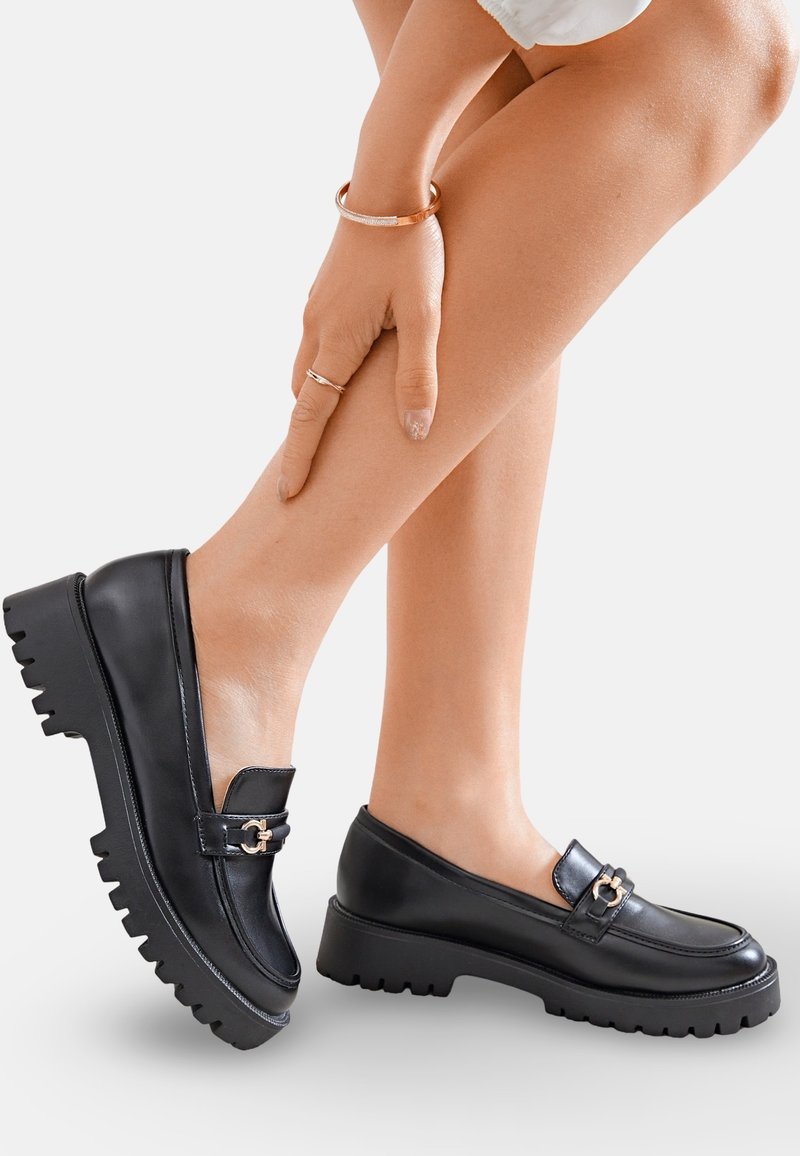 Mocassins en cuir noir avec une semelle épaisse, dotés d'un accent en métal doré sur le dessus. Texture lisse avec un design à bout rond.