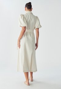 Beige jurk met pofmouwen, een kraag, een getailleerde taille en een lengte tot de middenkuit. Gemaakt van lichtgewicht stof met een gestructureerde afwerking.