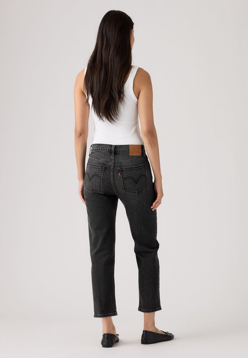 Black denim jeans with a straight-leg fit, mid-rise waist, and classic back pockets. Features a brown leather patch at the waistband.
