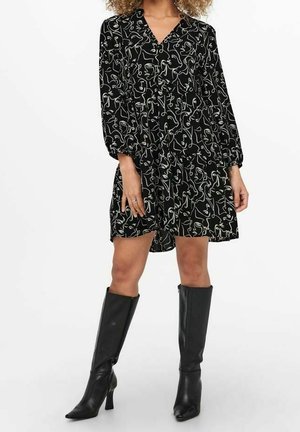 Robe noire avec un motif abstrait blanc, manches longues ballon, design enroulé et lien à la taille, associée à des bottes noires jusqu'aux genoux.