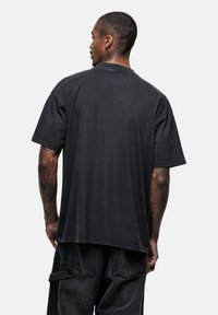 Czarna, oversize koszulka z krótkim rękawem, okrągłym dekoltem i luźnym krojem, z miękką teksturą i subtelnymi detalami w szyciu.