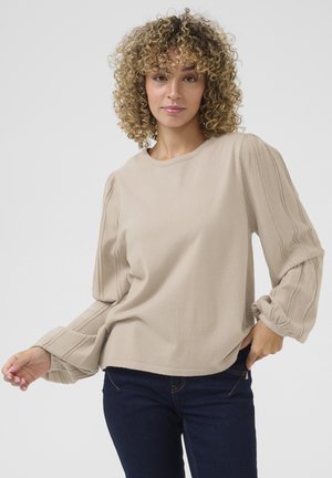 Sweatshirt en maille beige avec manches bouffantes, présentant une texture en côtes verticales. À associer avec un jean bleu foncé, coupe décontractée, design col ras du cou.